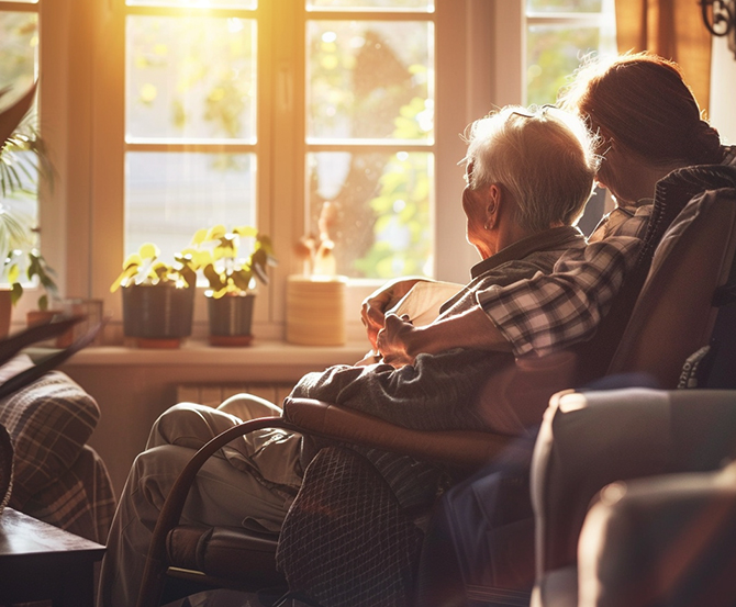 Sunset time with elderly couple embracing in a chair looking out the window.
